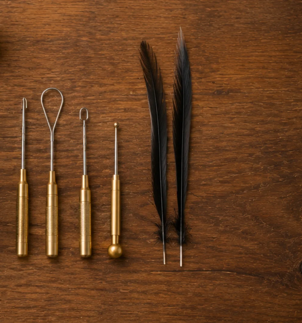 Brass-handled tying tools laid beside two dark hackle feathers on a wooden bench